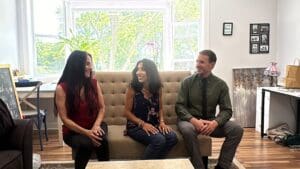 Three people sitting on a couch in front of a window.